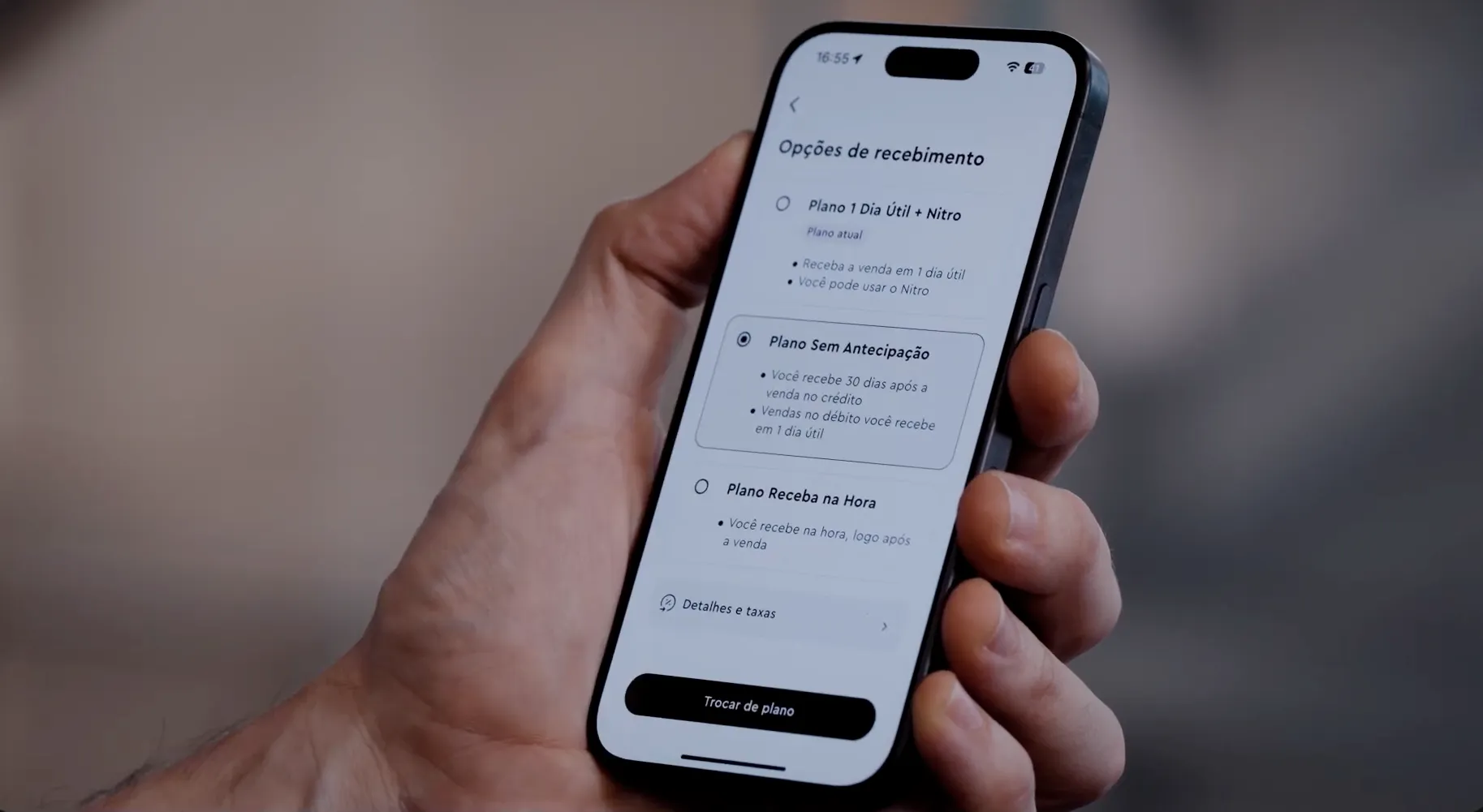 Hand holding smartphone showing options for receiving payments with three plan choices in Portuguese.