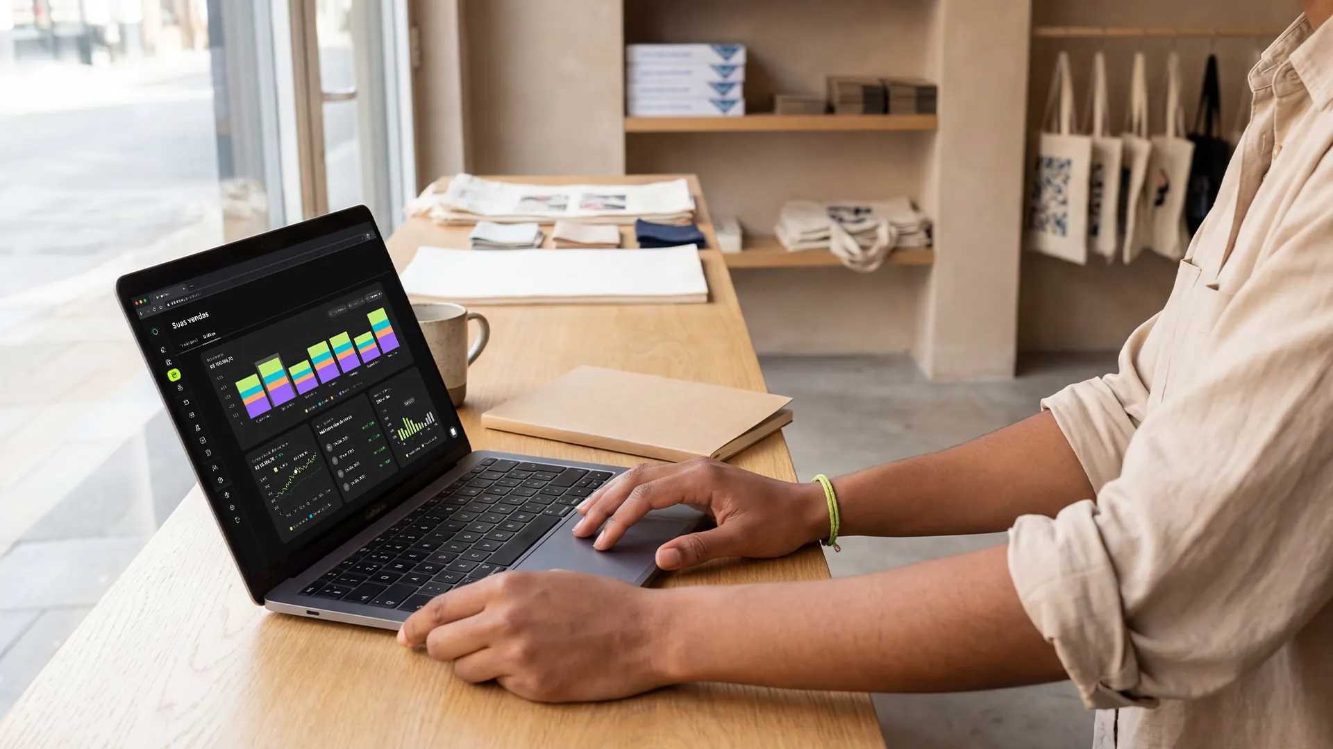 Person using a laptop at a wooden counter with sales data charts on the screen in a store.