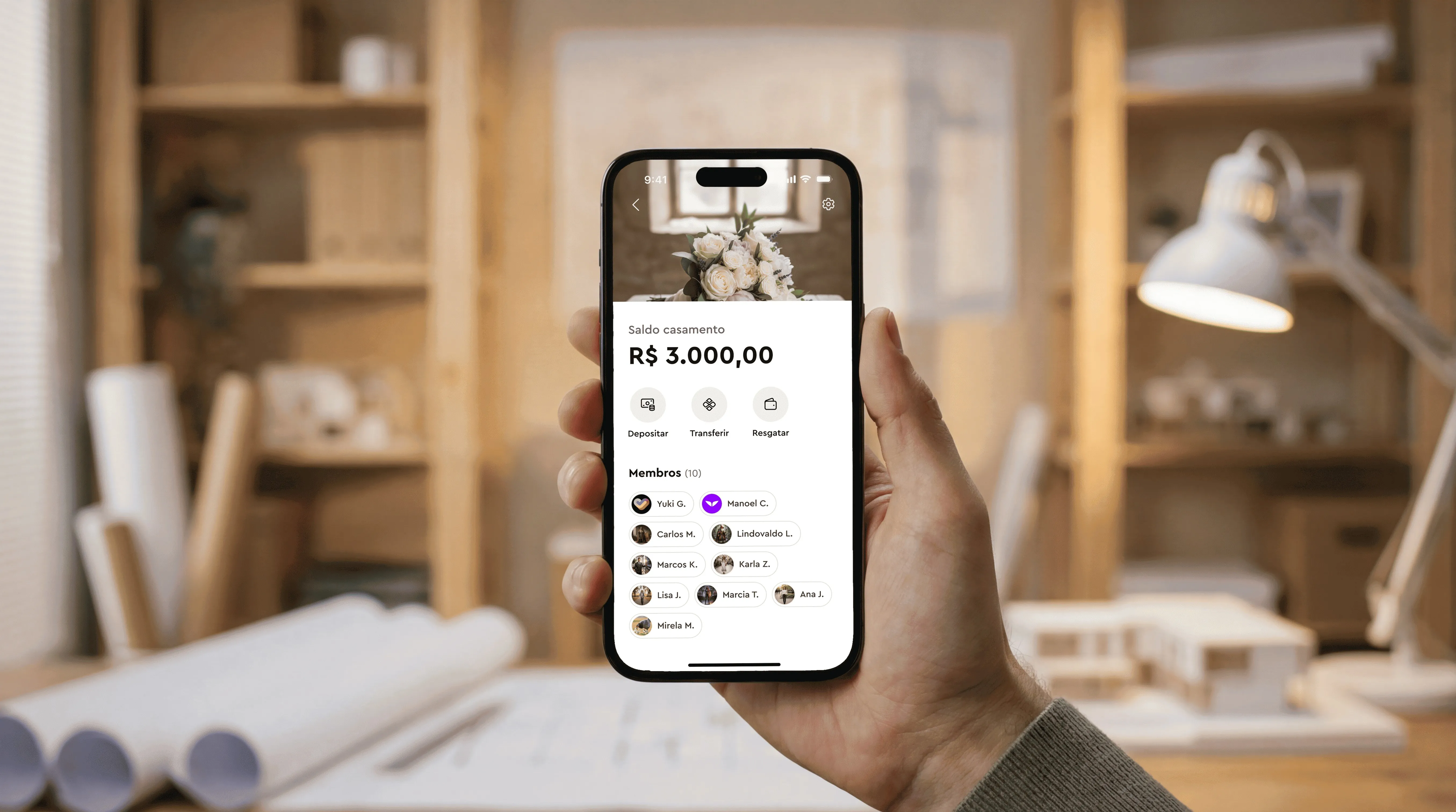 Hand holding a phone showing a wedding fund app with balance R$ 3,000 and member list.