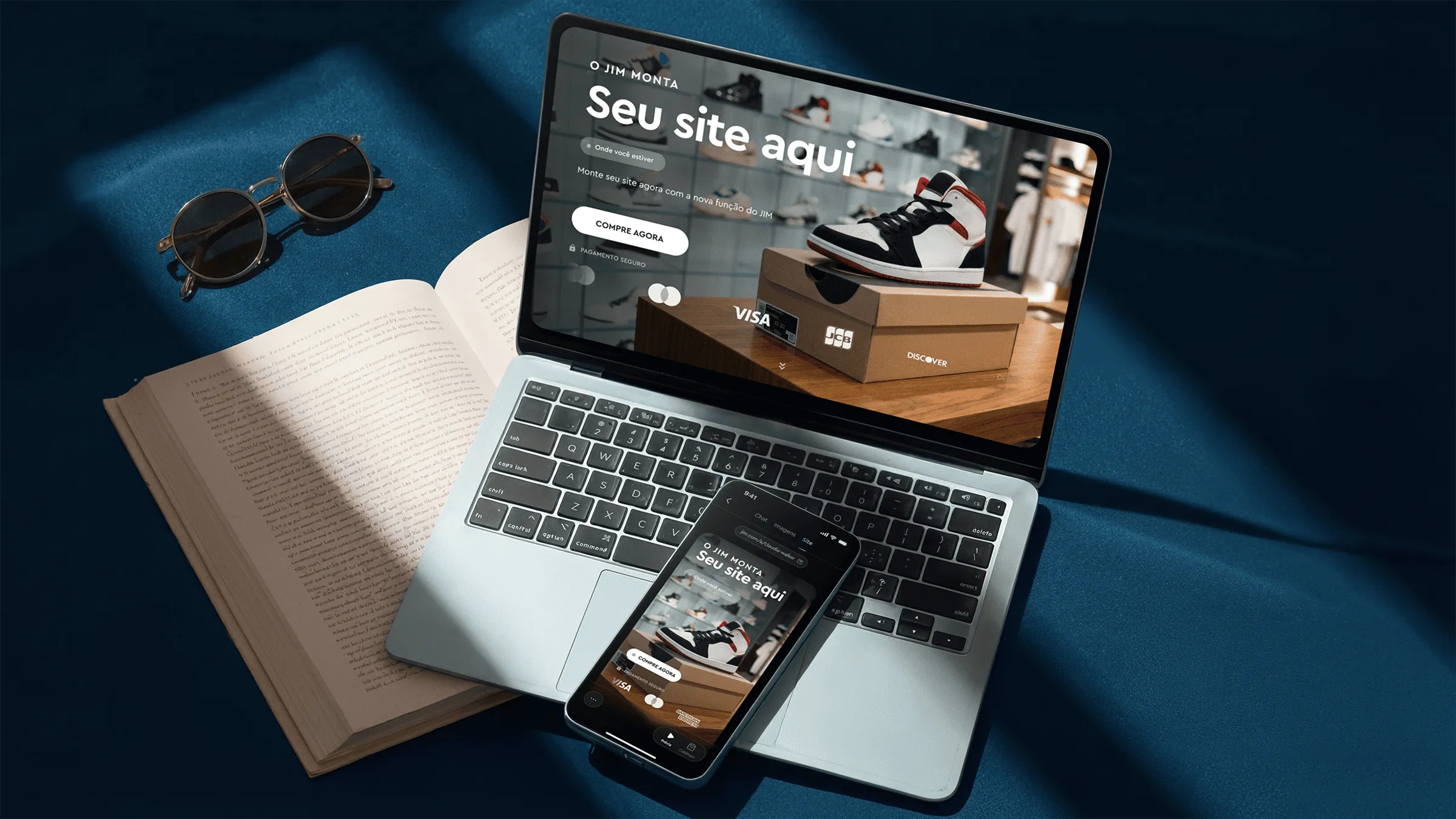 Laptop and smartphone display a shoe store website on a blue surface with open book and sunglasses.