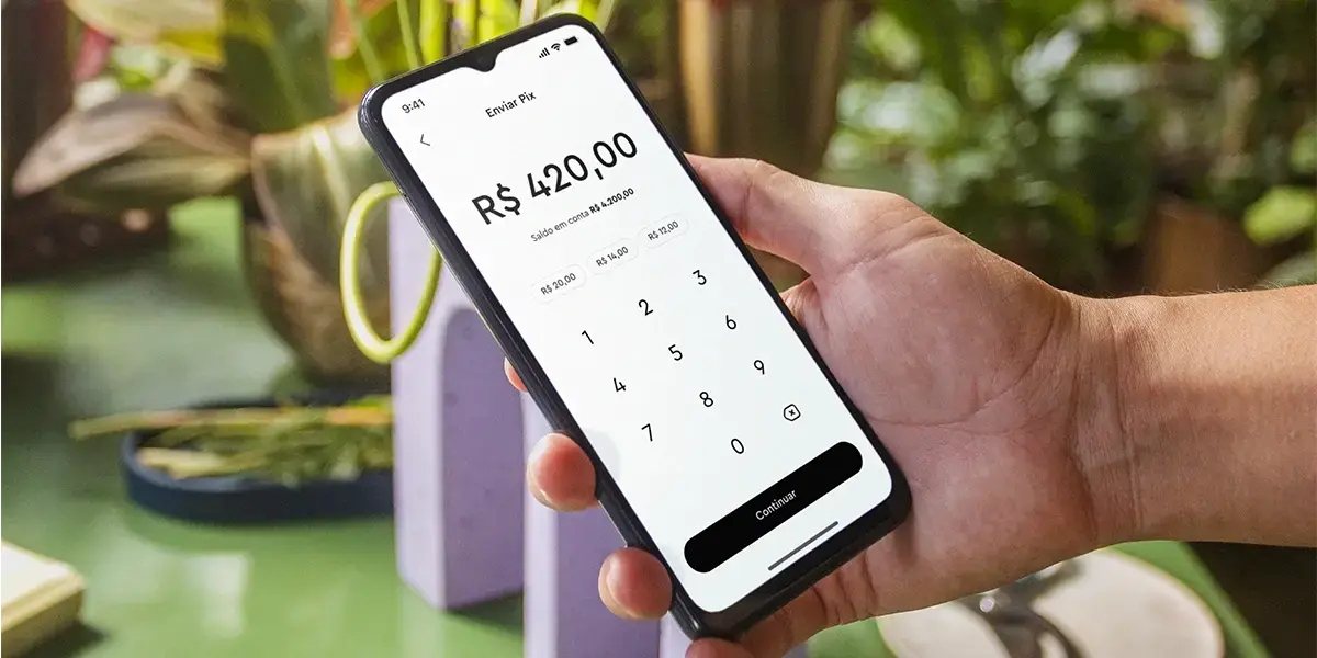 como fazer pix para outra pessoa: imagem mostra mçao segurando smartphone, cuja tela mostra a interface do app