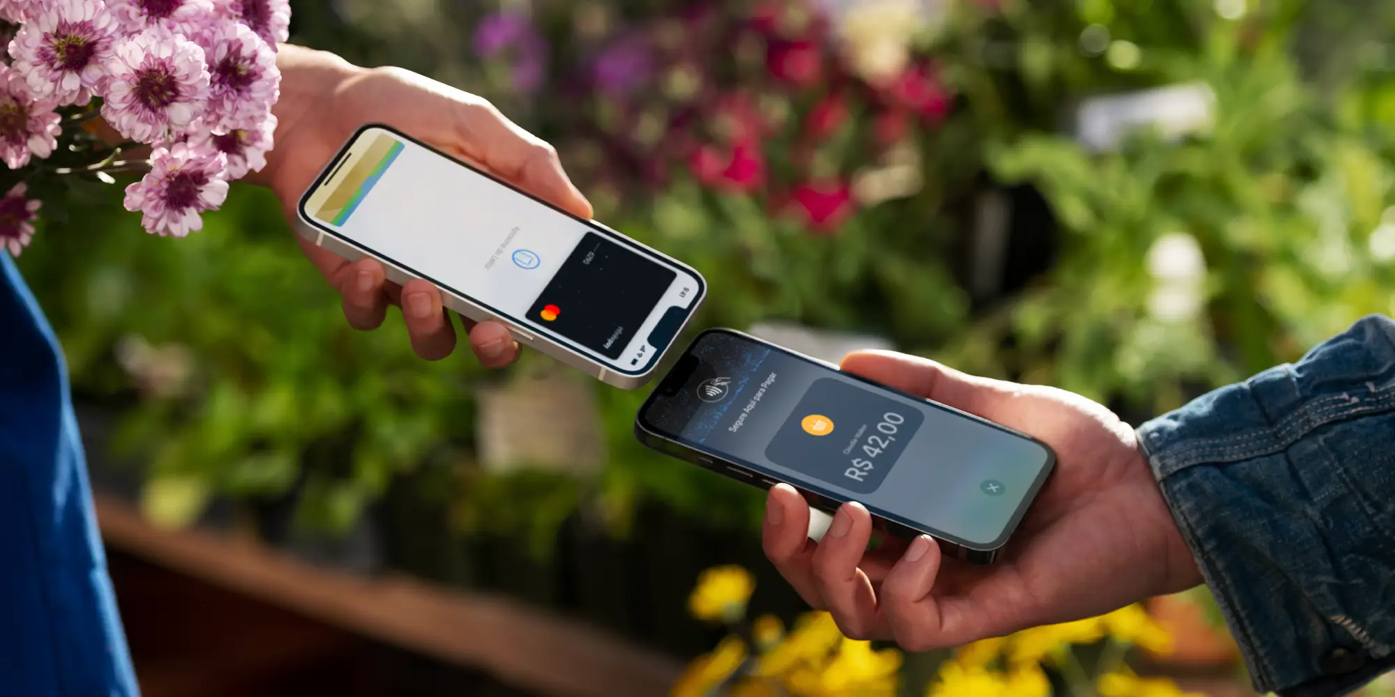 Imagem que ilustra artigo sobre Tap to Pay no iPhone com InfinitePay mostra uma pessoa aproximando um iPhone de outro iPhone para fazer pagamento por aproximação, ao fundo, uma banca de flores