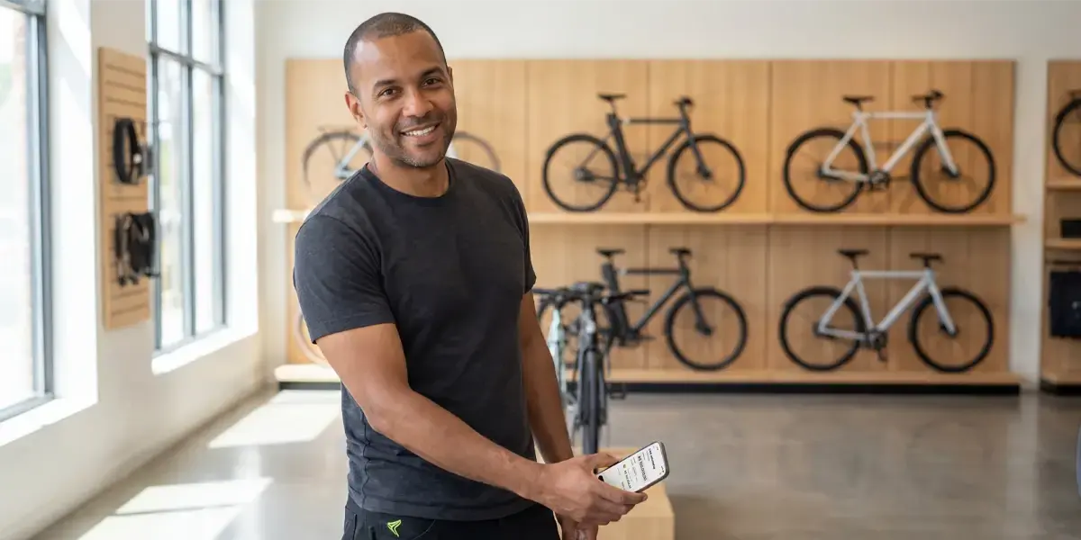 Homem sorridente em loja de bicicletas analisando no celular quanto rende 10 mil no CDB.