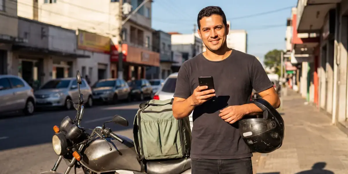 Entregador com celular na mão conferindo investimentos e analisando se cdb é renda fixa.