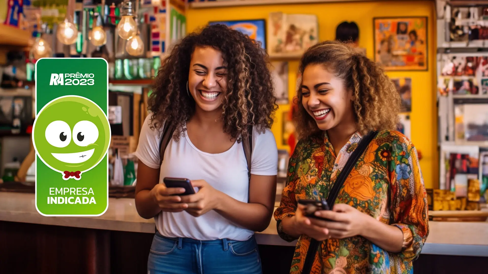 Duas mulheres negras sorrindo com celular nas mãos. A mulher a esquerda está com cabelo crespo com luzes loiras e preso, sua camisa é longa e estampada em tons laranjas e verdes. A outra possui cabelos crespos soltos, ela está de camisa branca e calça jeans azul. No canto da foto, há o símbolo do RA100 conquista da InfinitePay, por ser a empresa de maquininha mais bem avaliada na sua área de maquininha de cartão 