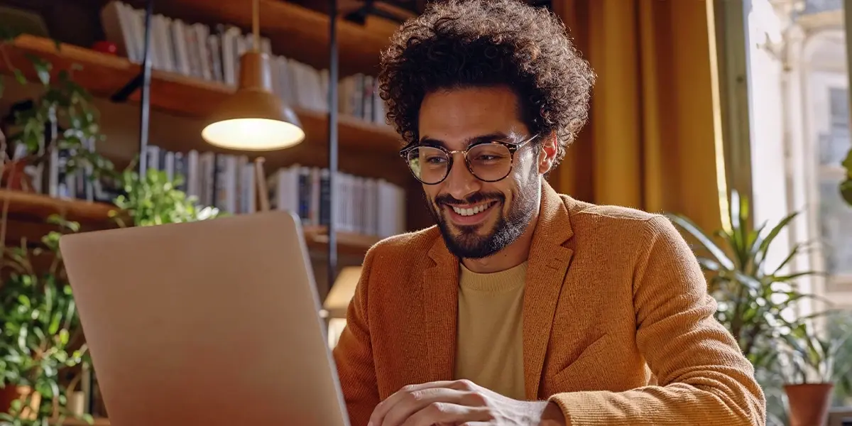 Homem sorrindo usa laptop em ambiente de trabalho, pesquisando sobre melhores plataformas de pagamento.