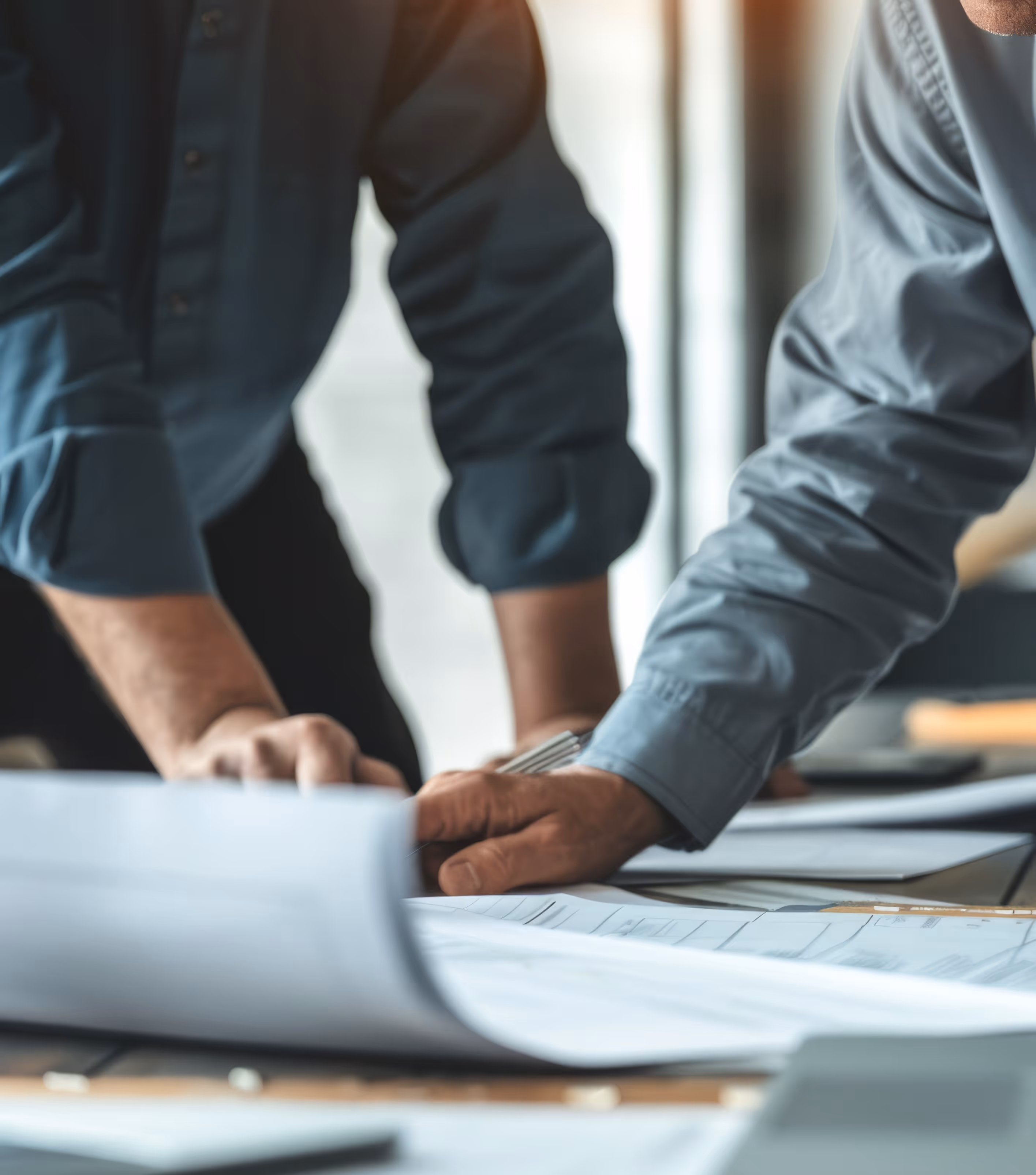 Two people reviewing and discussing architectural or engineering blueprints on a table.