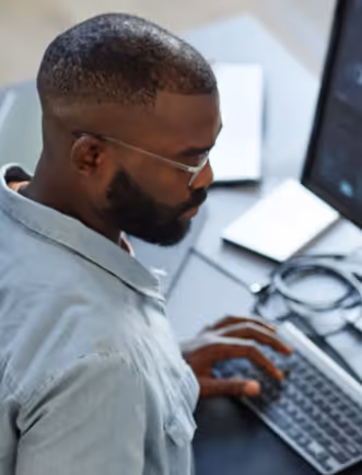 Man with glasses and beard typing on a computer keyboard at a desk.
