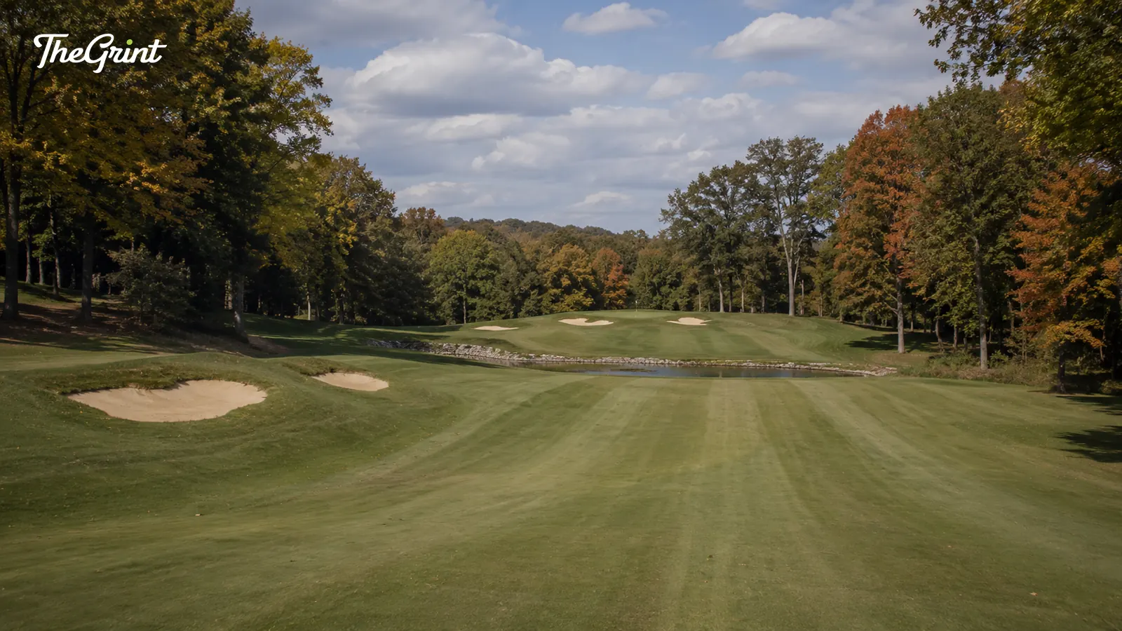 Parkland golf fairway with bunkers and autumn trees under a blue sky