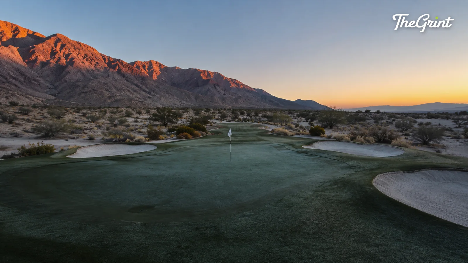 Desert golf green and bunkers at dawn with a red mountain range behind