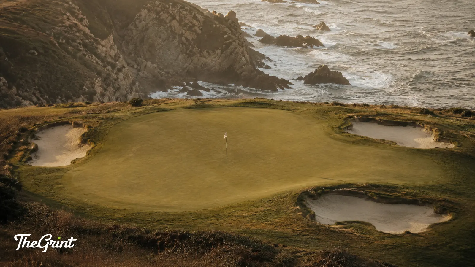 Elevated golf green ringed by bunkers above a rocky cove
