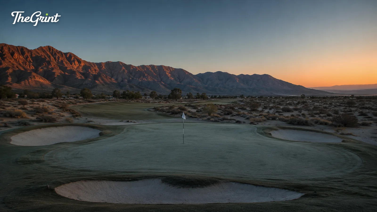 Desert golf green with bunkers at sunrise below red mountains