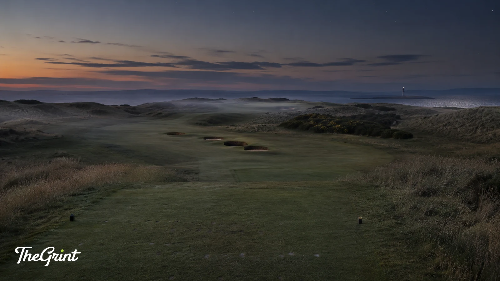 Links golf hole at dusk with pot bunkers, dune grass and a lighthouse on the coast behind