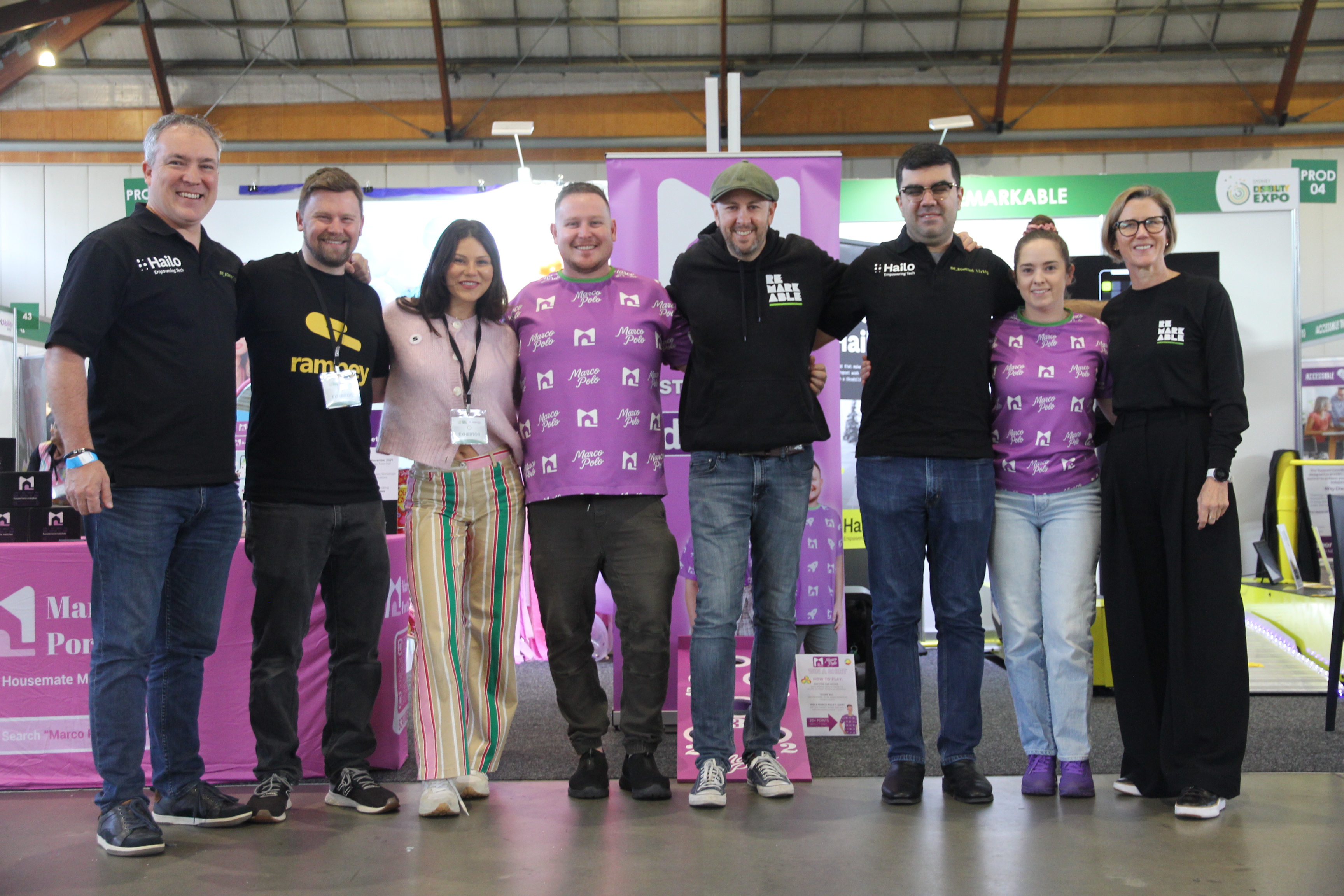 A group of eight people together at the Sydney Disability Expo, standing in front of a purple Remarkable booth display.