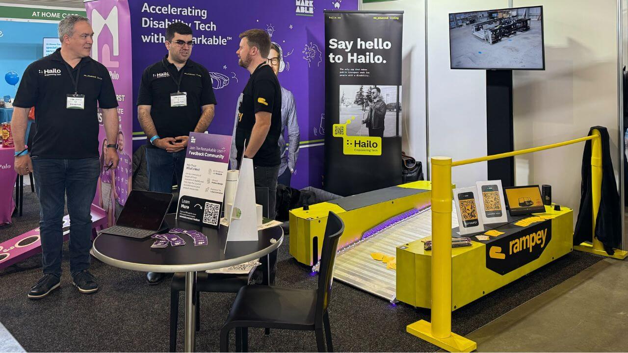 Hailo and Rampey teams talking with attendees at their joint booth during the Sydney Disability Expo 2025, with Rampey's accessible train ramp and branded display visible.