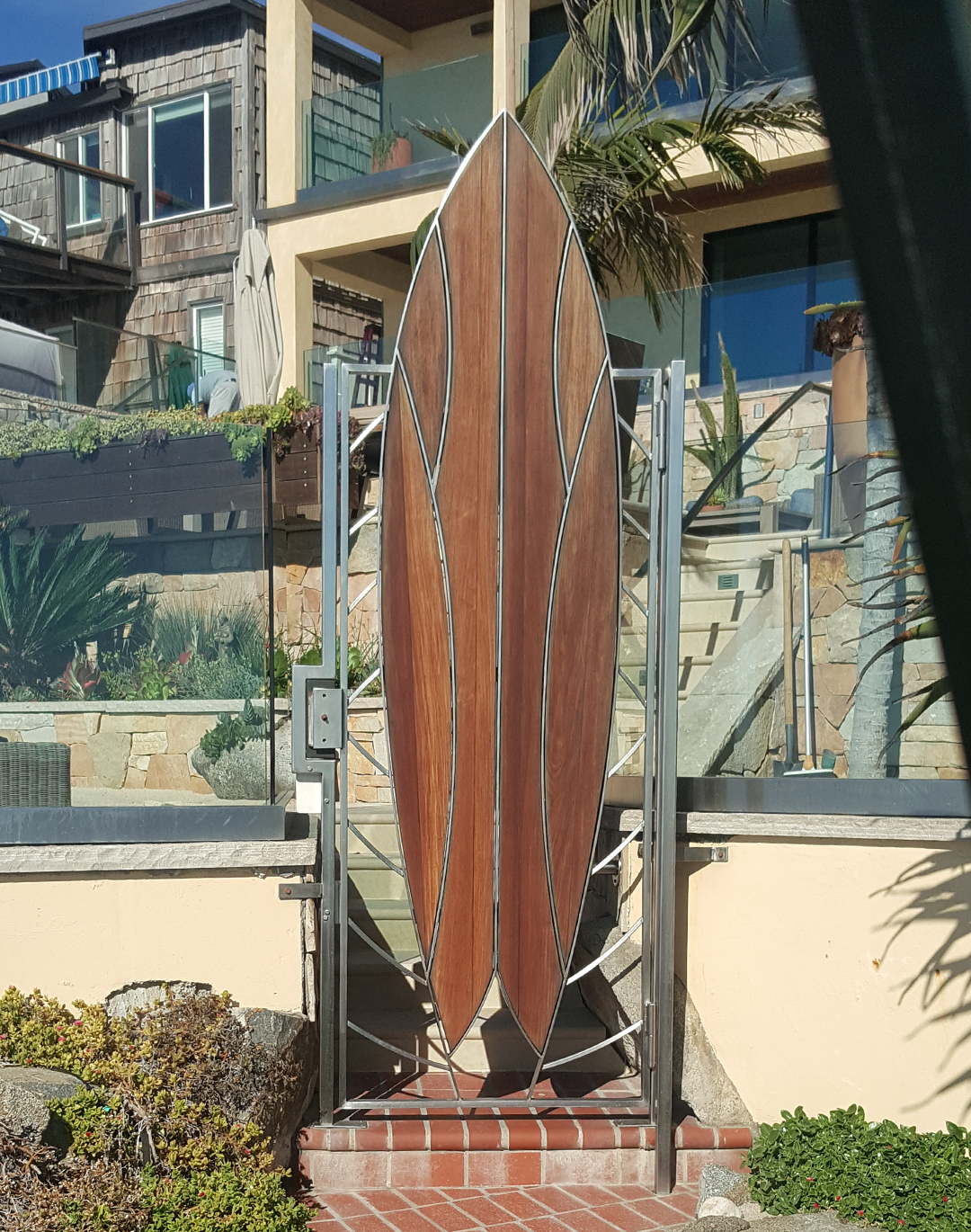 Custom steel entry gate shaped like a surfboard with wood panels