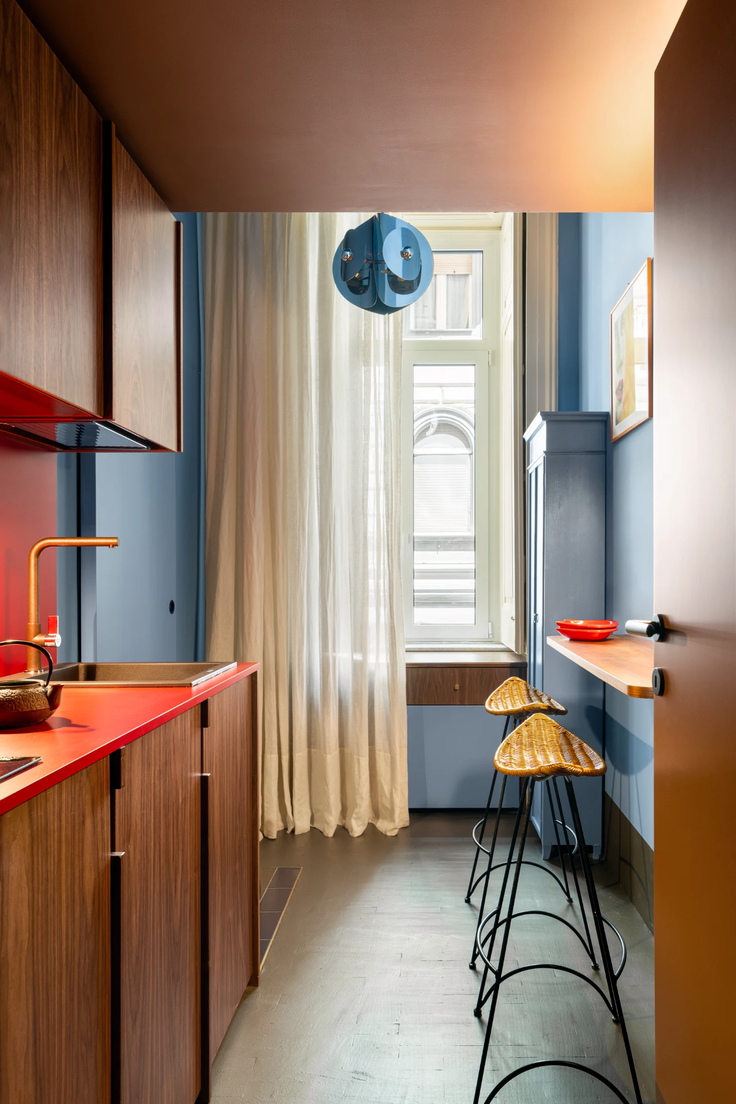 The kitchen, an essential part of Nicola and Chicco's secondary residence, comprises of rich wooden joinery, a set of stools from Tom Dixon's 1980s Banana Chair series for Cappellini, and a 1970s style painted metal pendant light.