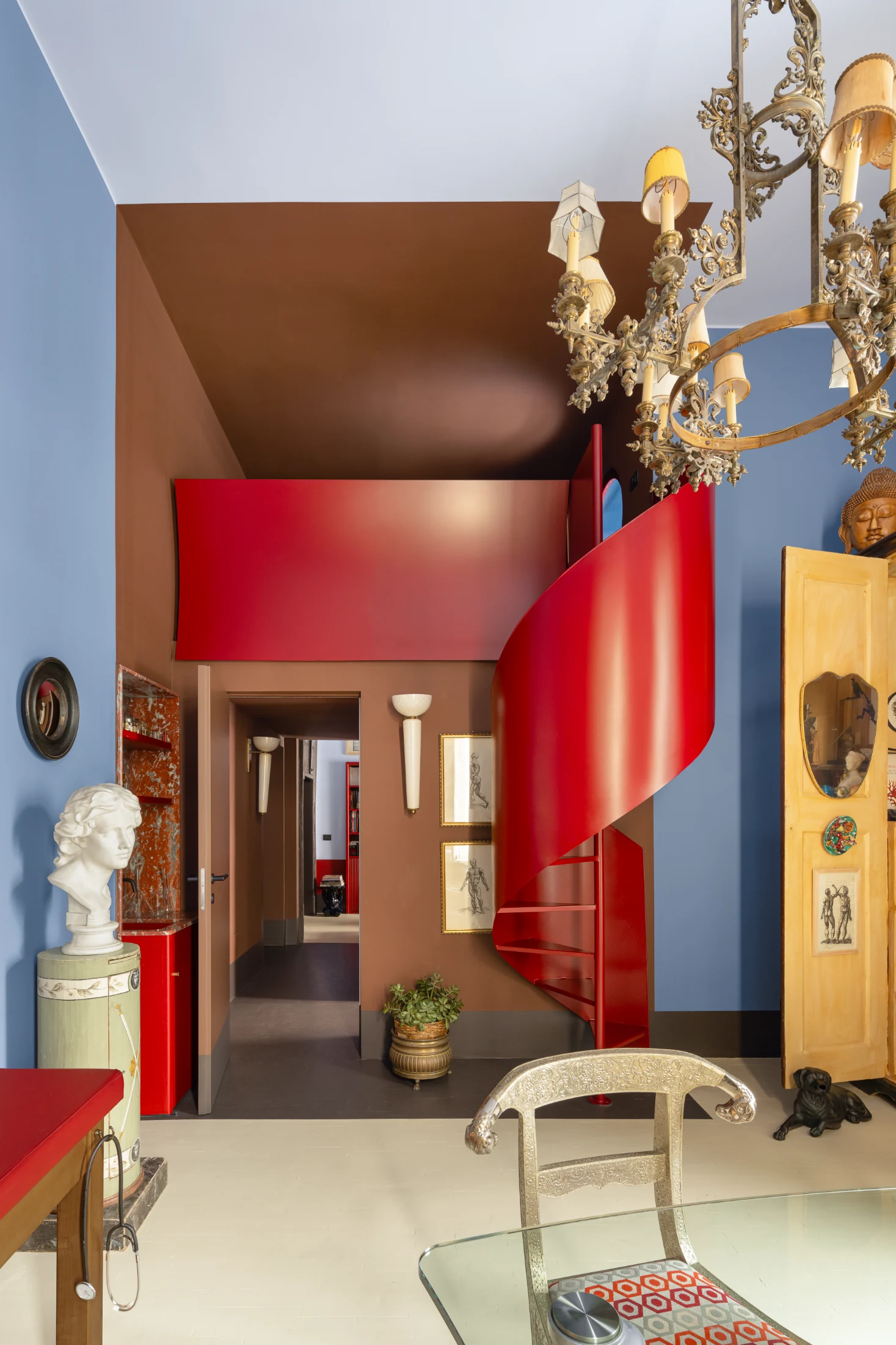 The red metal spiral staircase is one of Poerio's most striking features, connecting the lower level of the apartment to its mezzanine. The staircase offers a clear division between the medical practice space below and the private domain of the mezzanine l