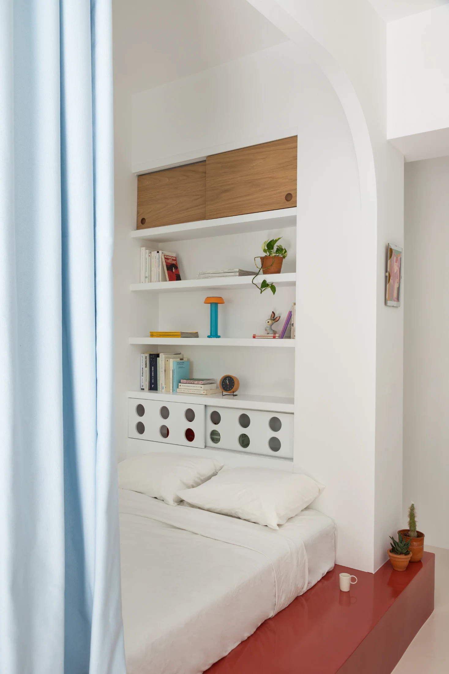 As well as being the apartment's sleeping area, the nook includes an integrated library and storage space above the bed.