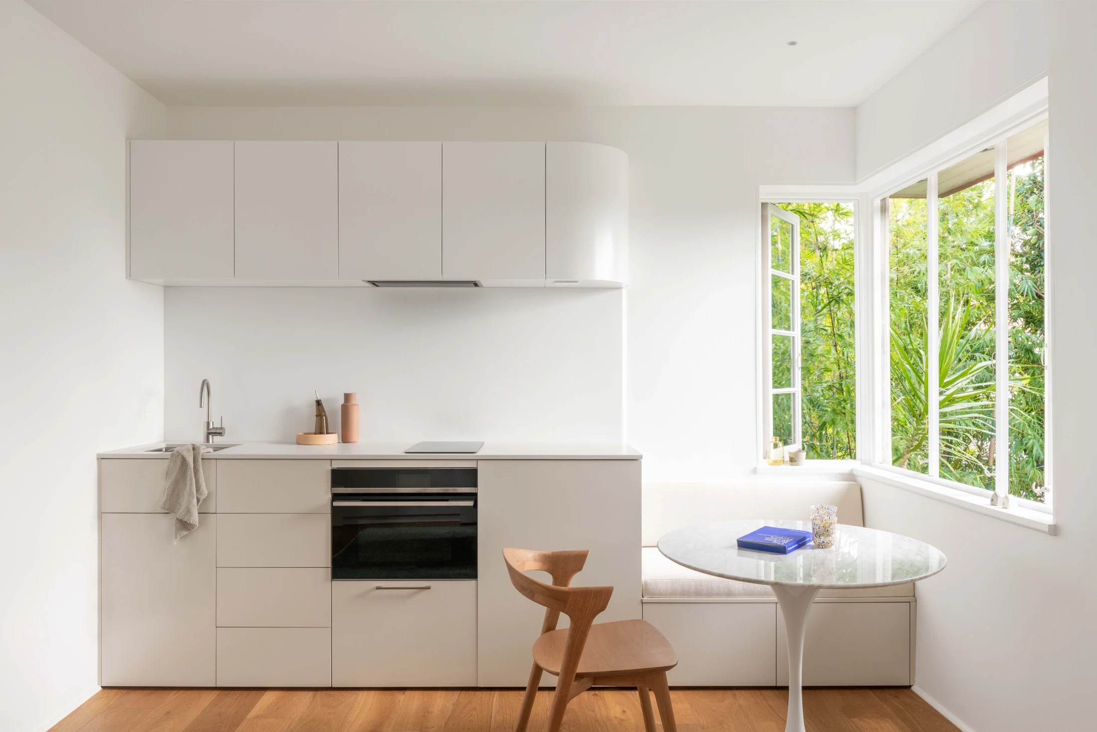 The unassuming white and light grey kitchen in The Slow Down Apartment designed by Brad Swartz perfectly integrates a large kitchen nook hugged by the dining sized corner windows. The nook is the perfect continuation of the kitchen space and includes built