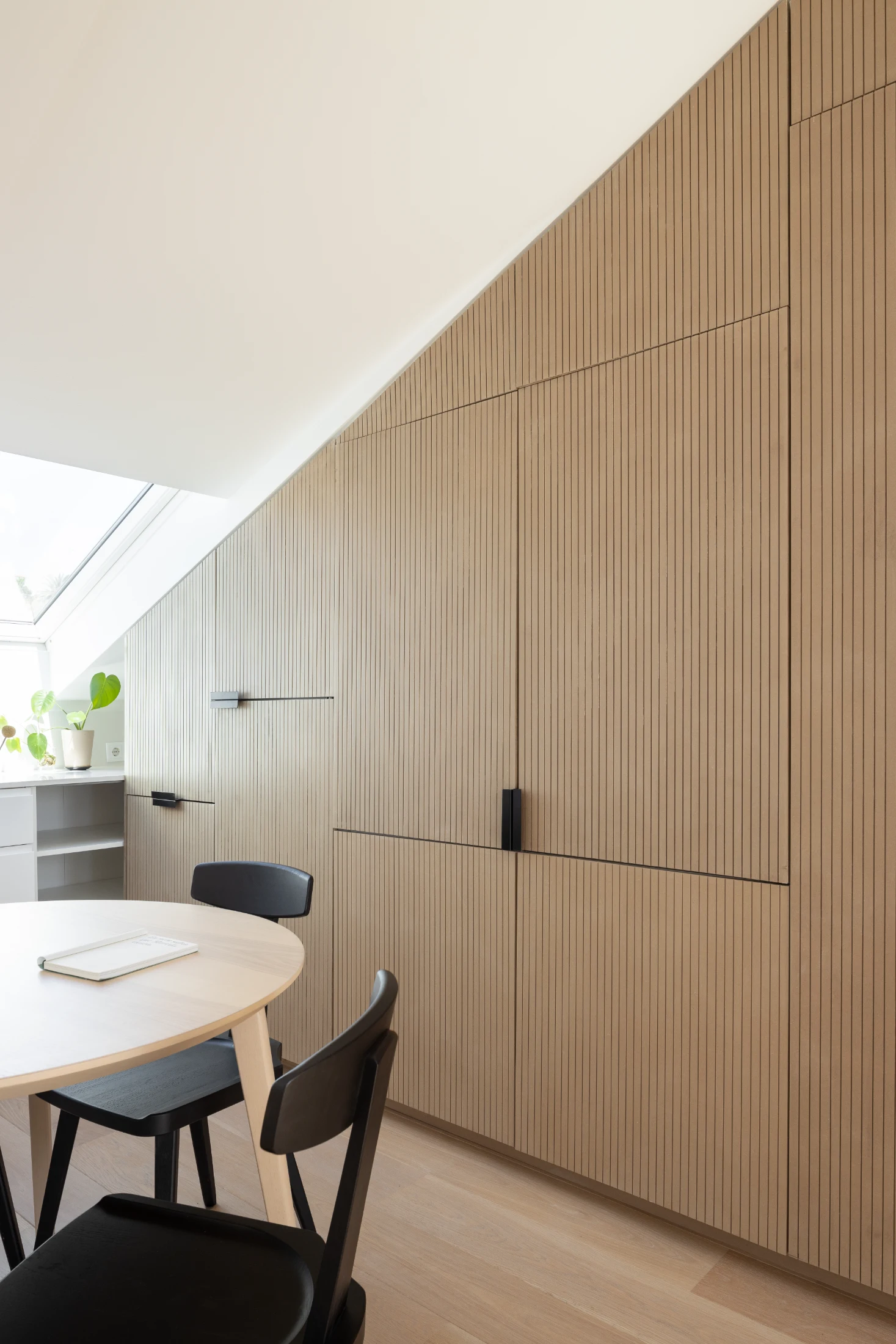 A pair of discreet pocket doors open and slide into a wall of joinery to reveal the kitchen in Marvila Attic designed by KEMA Studio. The whole setup includes a dishwasher, fridge, induction cooktop and a rangehood.