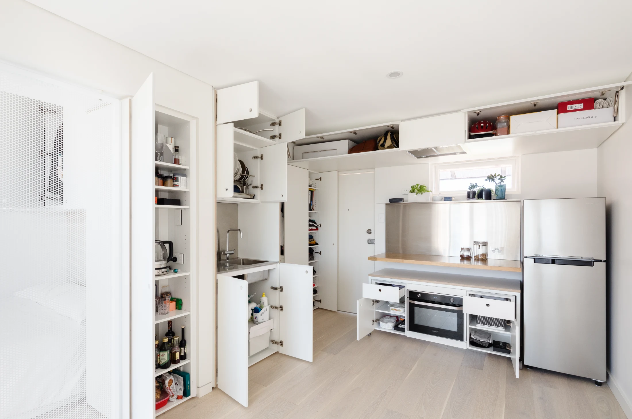 The extremely storage-efficient kitchen in Nicholas Gurney's 5S apartment design makes clever use of limited storage space. Featuring deep, narrow overhead storage and a stainless steel shelf that extends above the splashback, the design also includes a ro