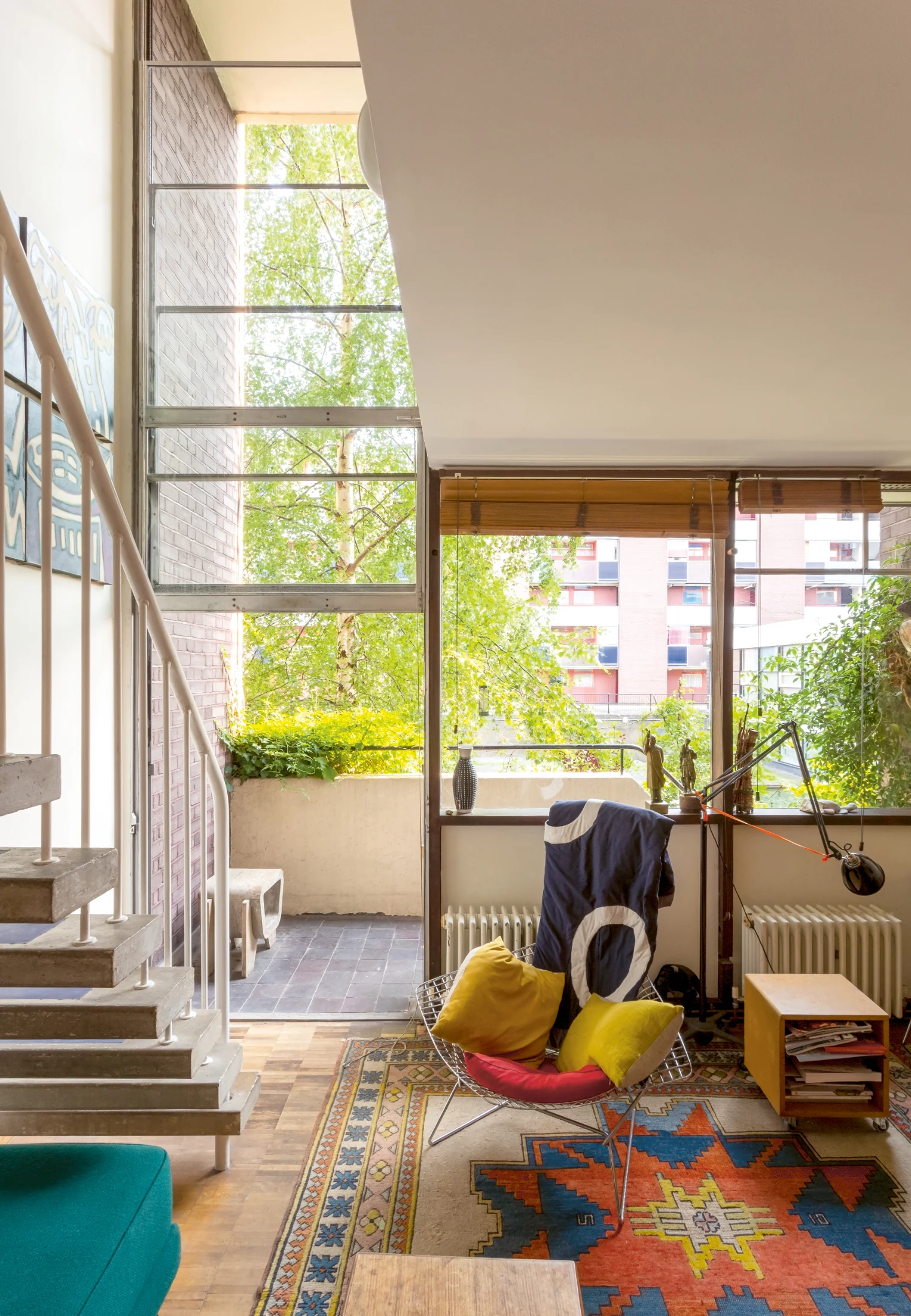 The living room of a ground floor maisonette in Bayer House, with views towards a balcony and communal gardens beyond. The double-height windows feature a vertically sliding door onto the balcony.