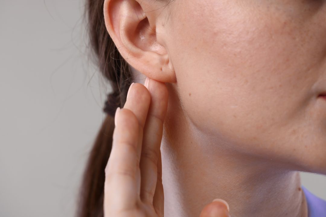 Close-up of a woman's ear with her hand gently touching the area behind it.