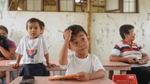 A child with a pencil, sitting at a desk, at school.