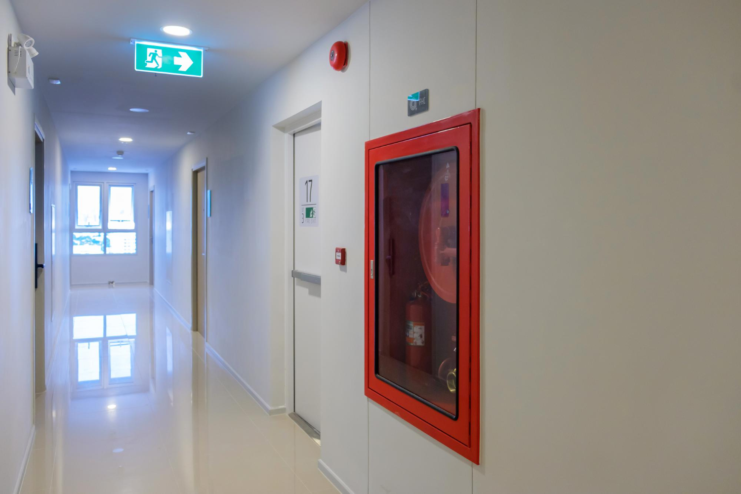 A hallway with a red framed fire hose on the wall.