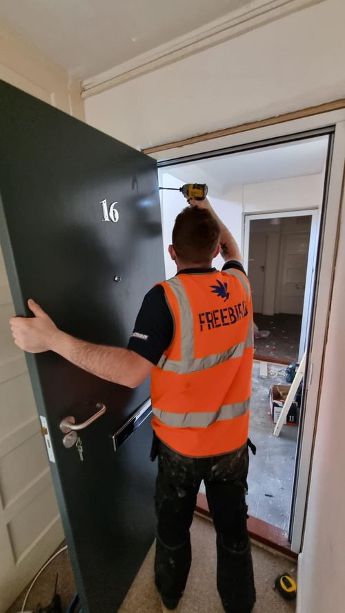 A man in an orange safety vest is installing a fire door.