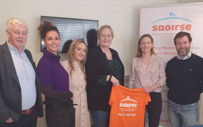 four women smiling holding an orange tshirt that says saoirse