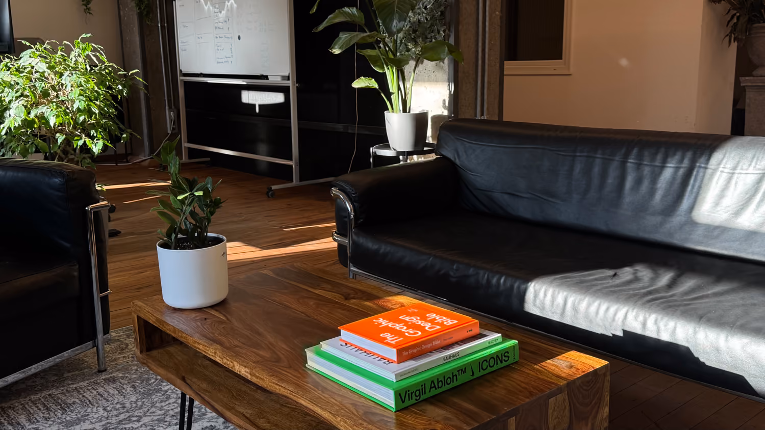 Modern Büro mit schwarzem Ledersofa, Holztisch, Pflanzen und Designbüchern auf dem Tisch.