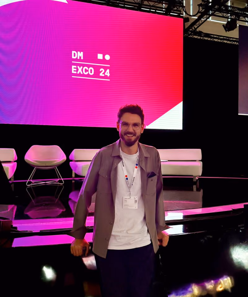 Ein lächelnder Mann mit Brille steht vor einer Bühne mit leuchtendem DMEXCO 24 Bildschirm.