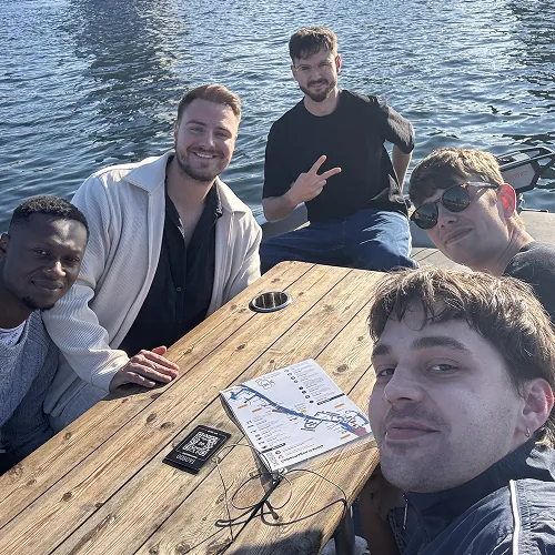 Team sitzt an einem Tisch auf einem Steg am Wasser