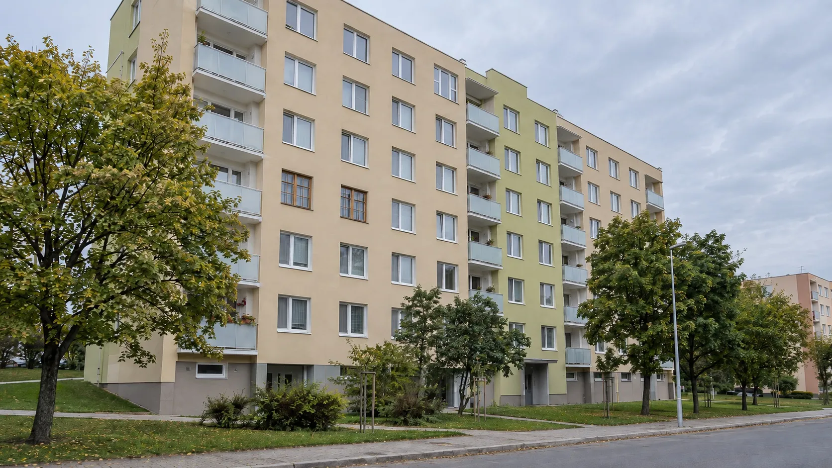 Zateplený panelový dom s béžovou a svetlozelenou fasádou a balkónmi so sklenými zábradliami. Väčšina okien je biela, dve okná na jednom poschodí majú hnedé rámy s iným členením.