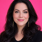 Portrait of Mel with long dark hair wearing a black top, smiling confidently against a bright pink background.