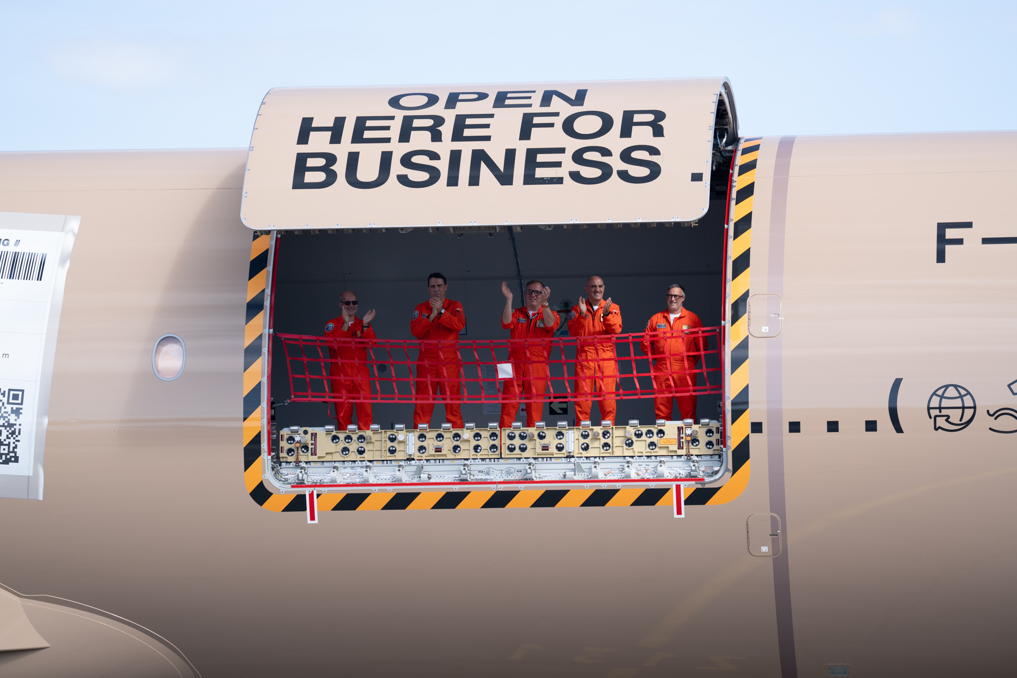 Five people in orange flight suits inside the open cargo door, several clapping.