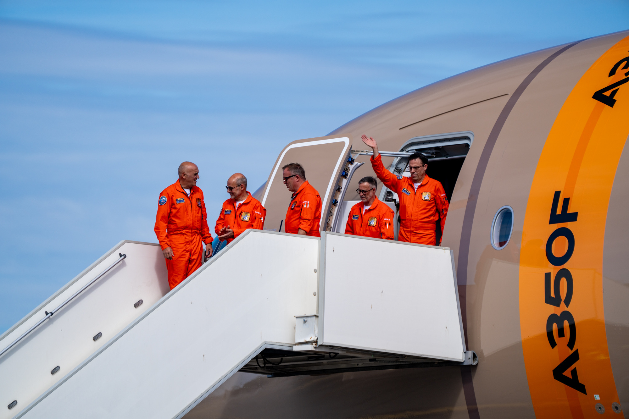 Five people in orange flight suits at the A350F's forward door and stairs.