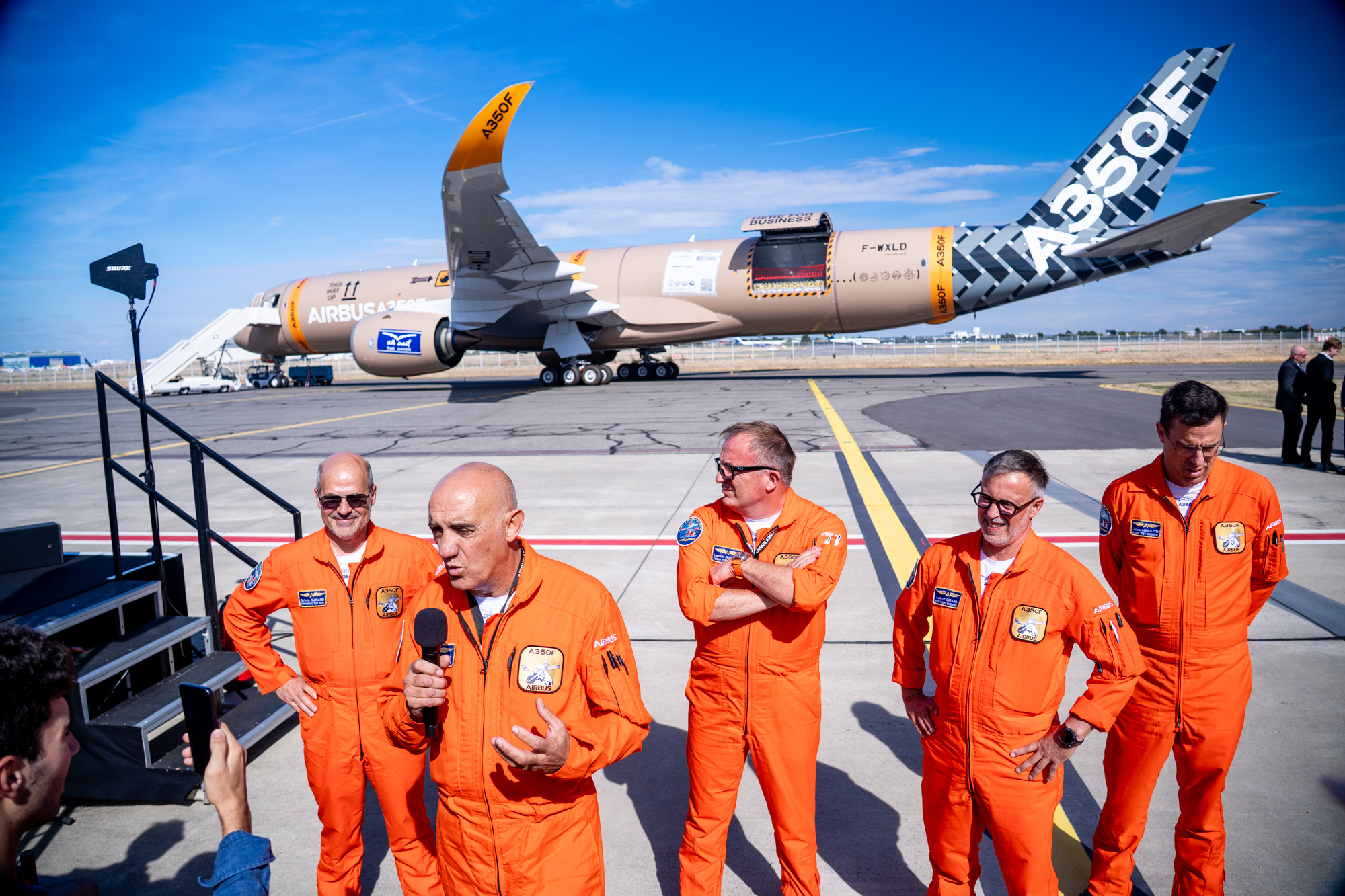 People in orange flight suits on the apron with the A350F behind them.