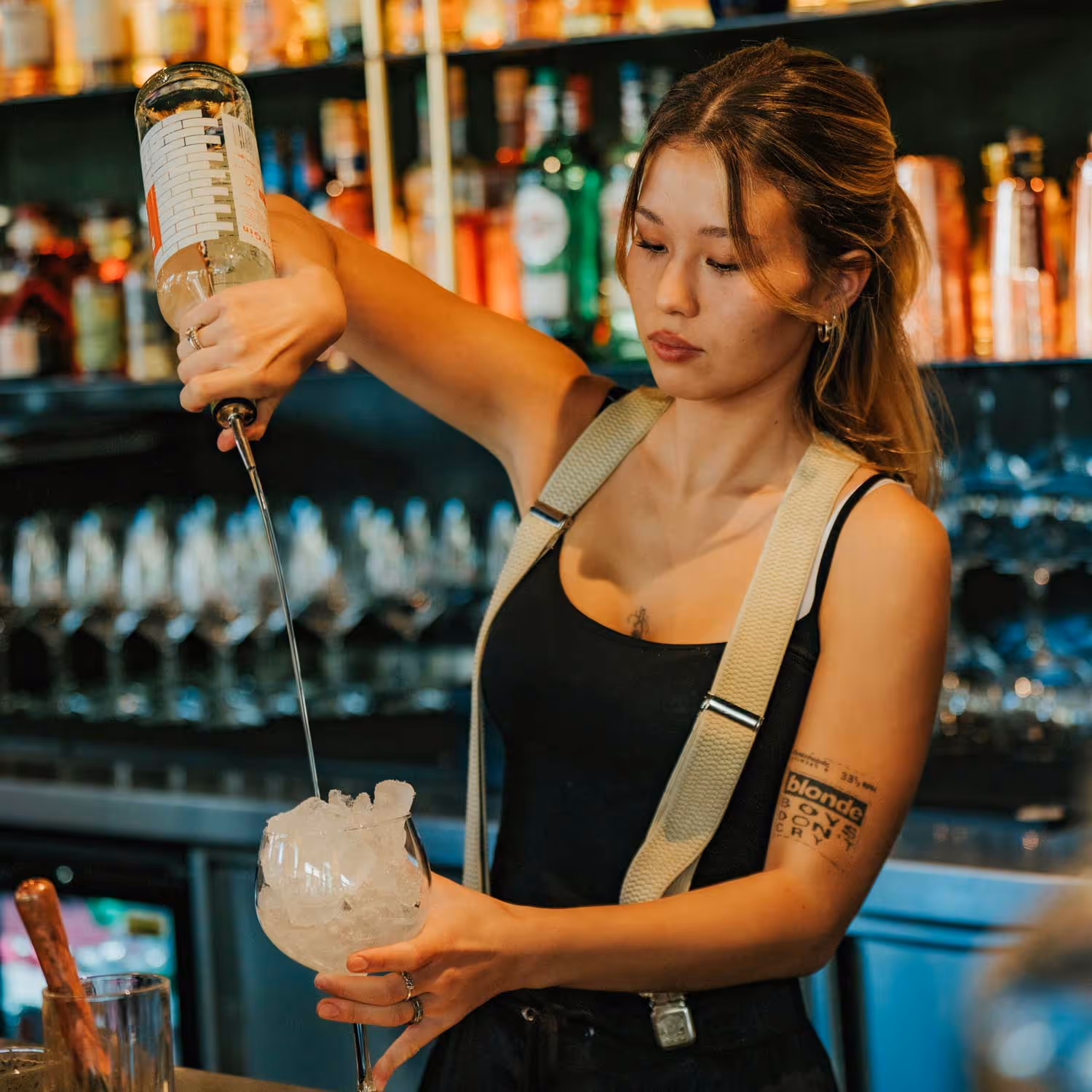 Barkeeperin füllt ein Glas mit Eiswürfeln hinter einer Bar mit Flaschen im Hintergrund.