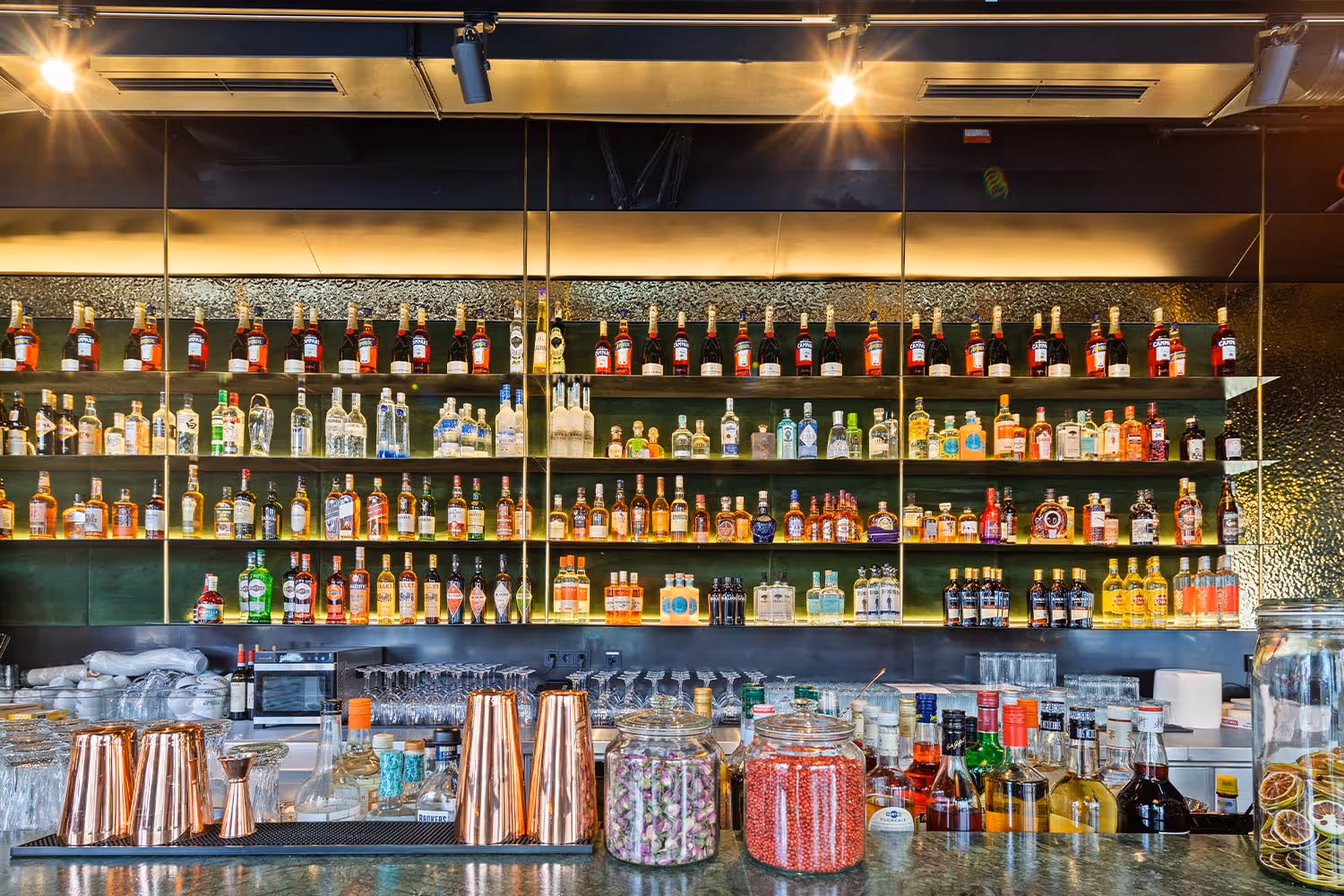 Bar mit mehreren Regalen voller verschiedener alkoholischer Getränkeflaschen und Gläsern auf der Theke.