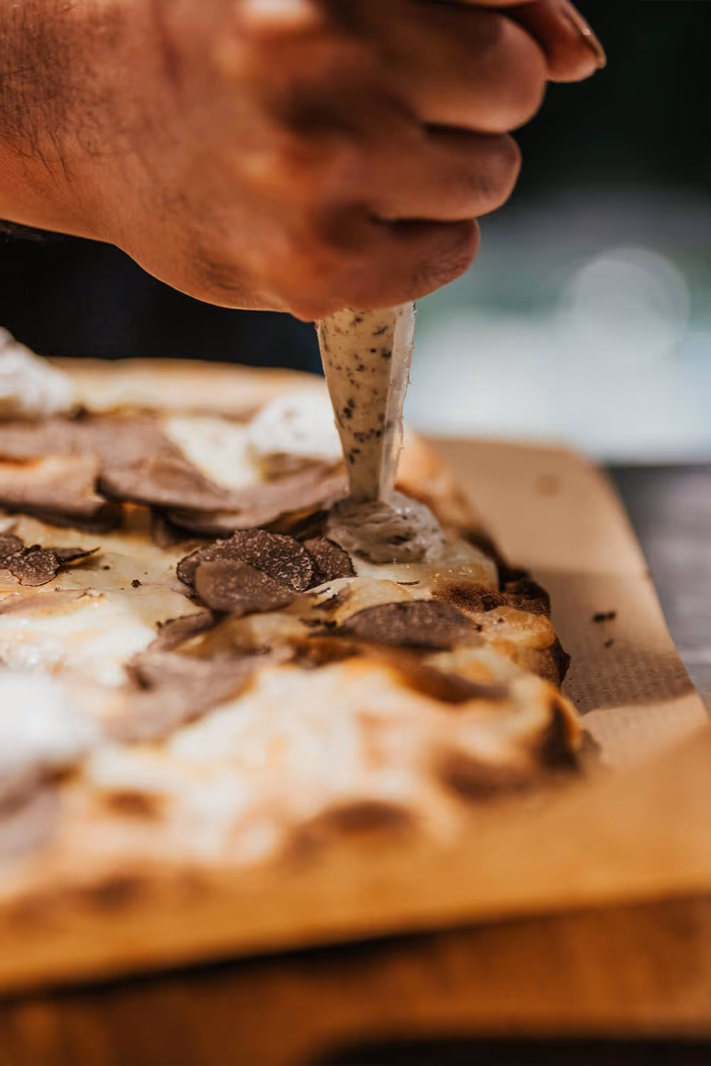 Hand spritzt cremige Sauce auf Pizza mit Trüffelscheiben.