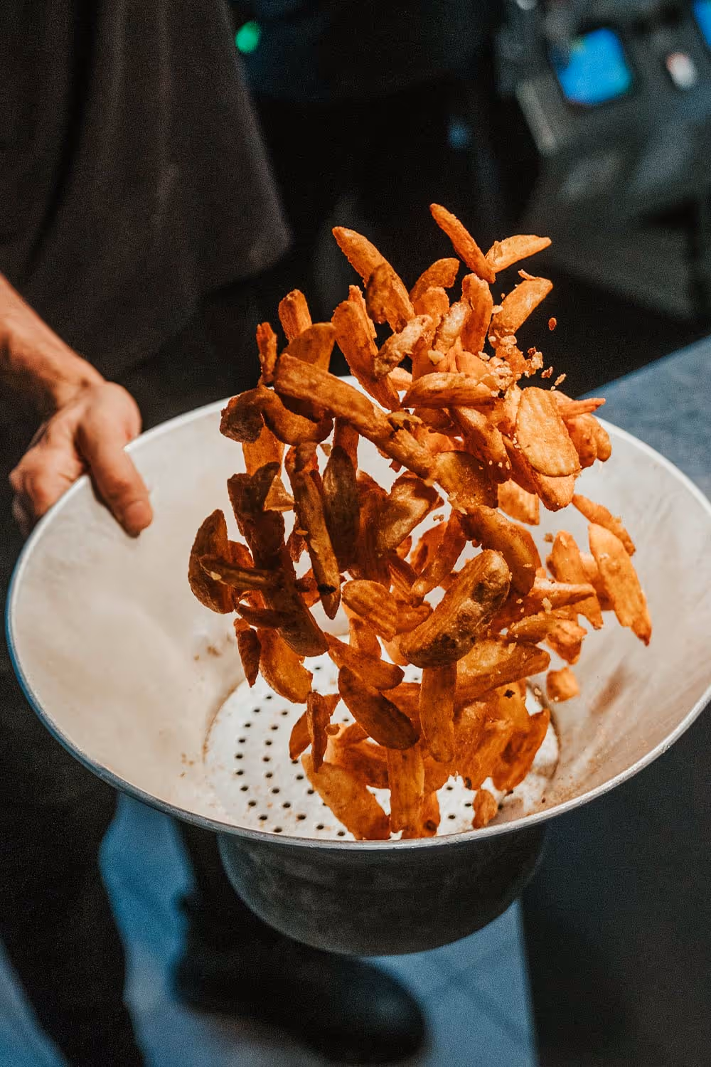 Hand schwenkt eine Schüssel mit knusprigen, goldbraunen Kartoffelchips in der Luft.