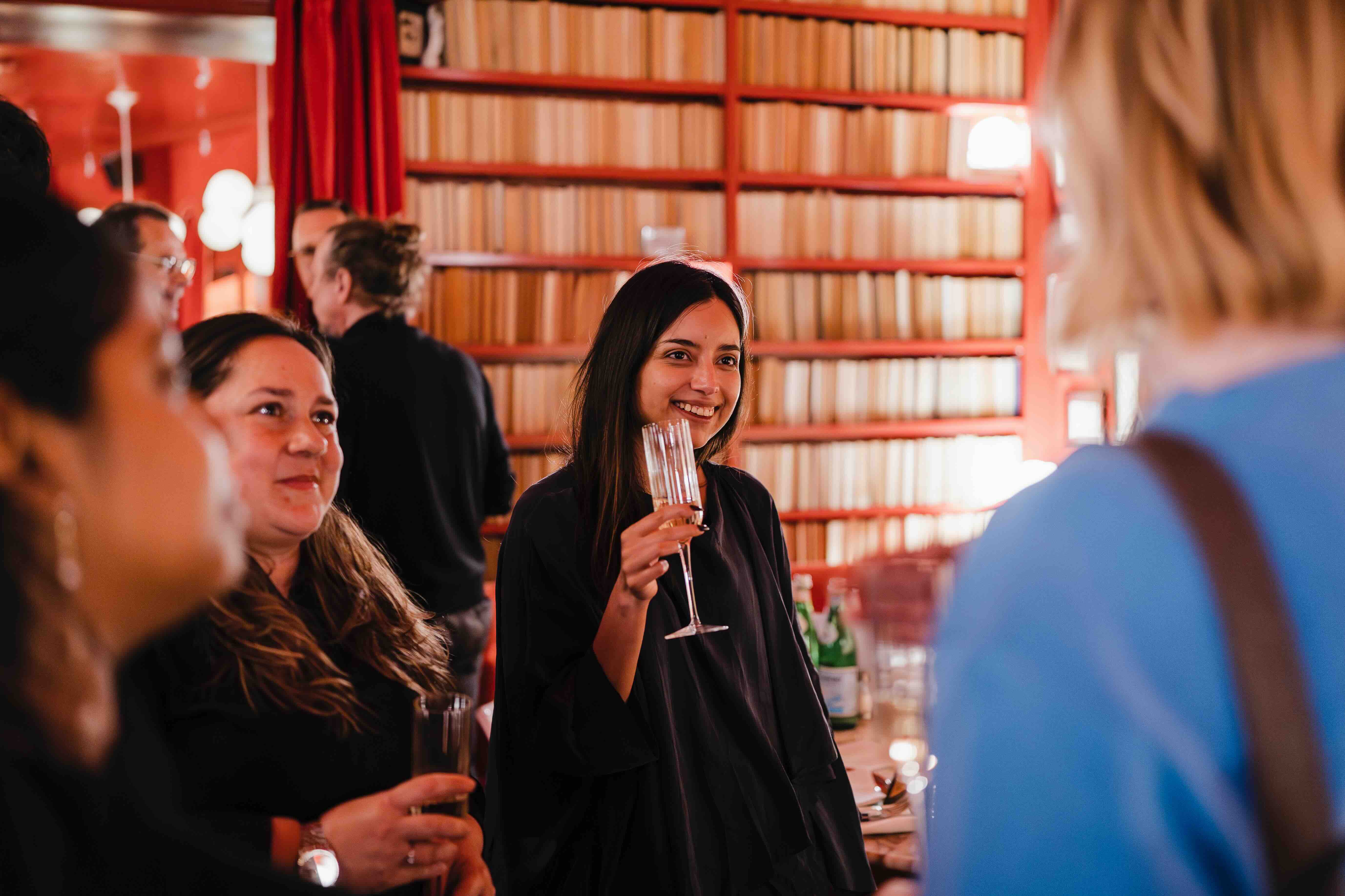 People networking in a cozy bar with bookshelves and red decor.
