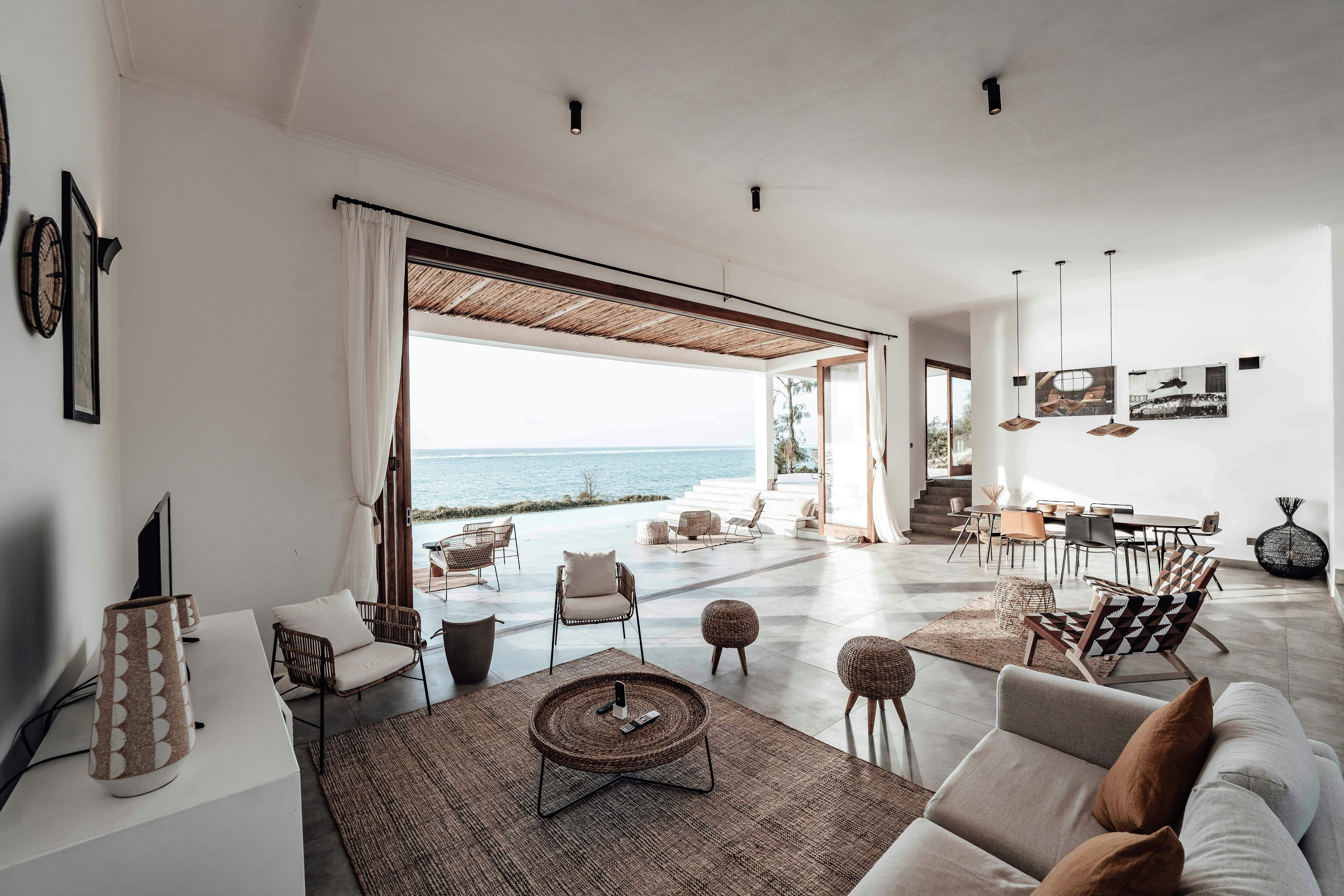 Modern coastal living space opening to a shaded terrace and ocean outlook through a large architectural opening. Credit: Photo by Keegan Checks: https://www.pexels.com/photo/interior-of-a-room-in-a-house-with-a-view-of-sea-12715501/