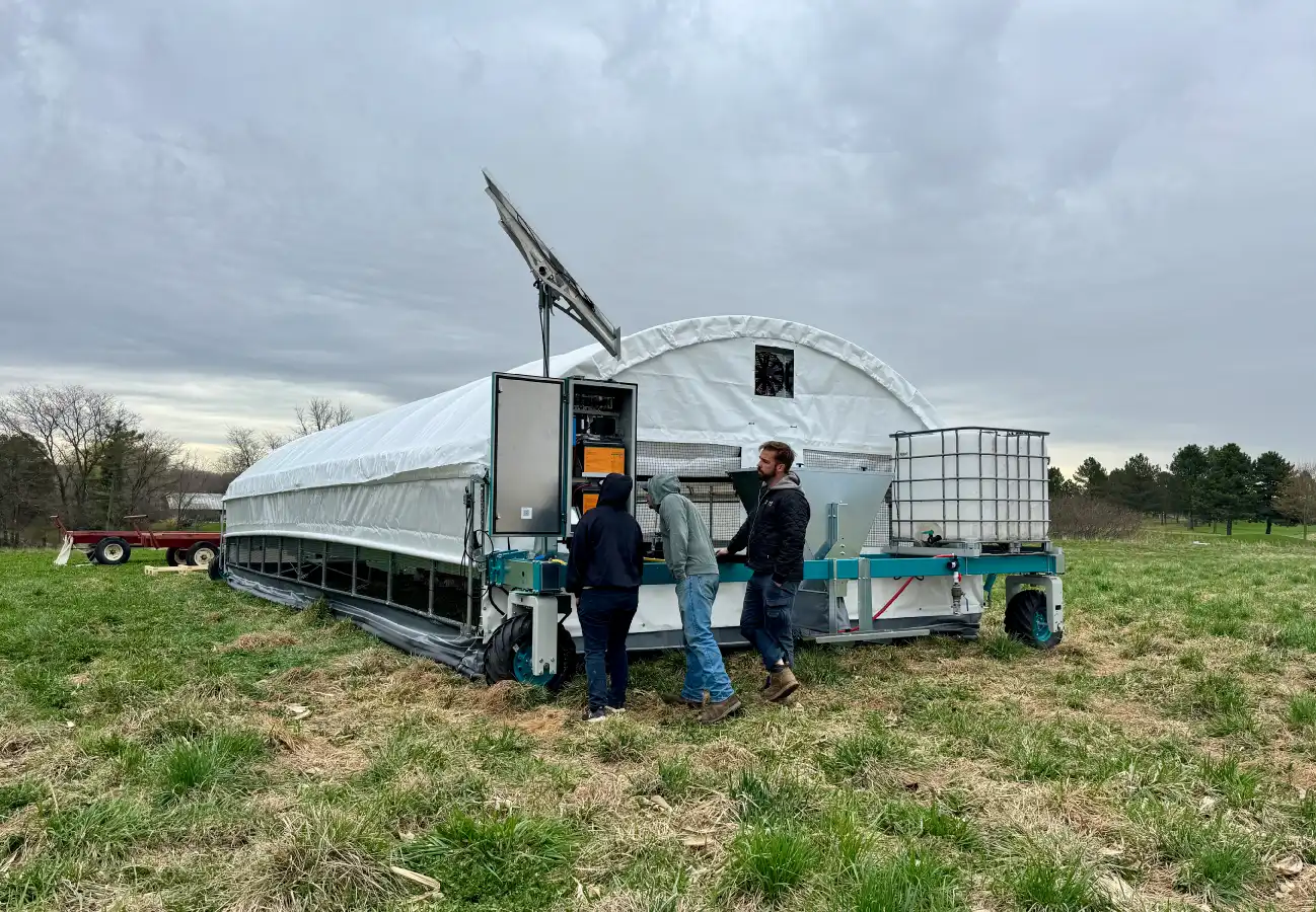 Three people gathered at the back of a ROVA|BARN 700, inspecting the control panel and solar-powered system.
