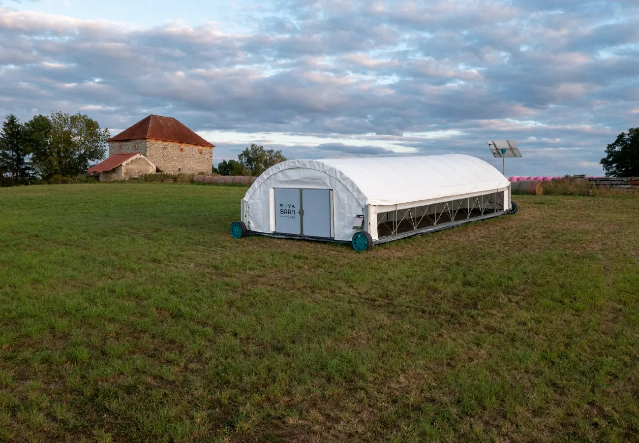 UKKÖ Robotics ROVA|BARN mobile poultry barn on a grassy field in Czechia, with a historic stone farm building and cloudy sky.