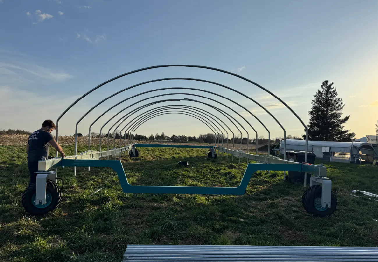 Farmer assembling the steel frame of a UKKÖ mobile poultry barn in a pasture, showing modular construction and durable design.