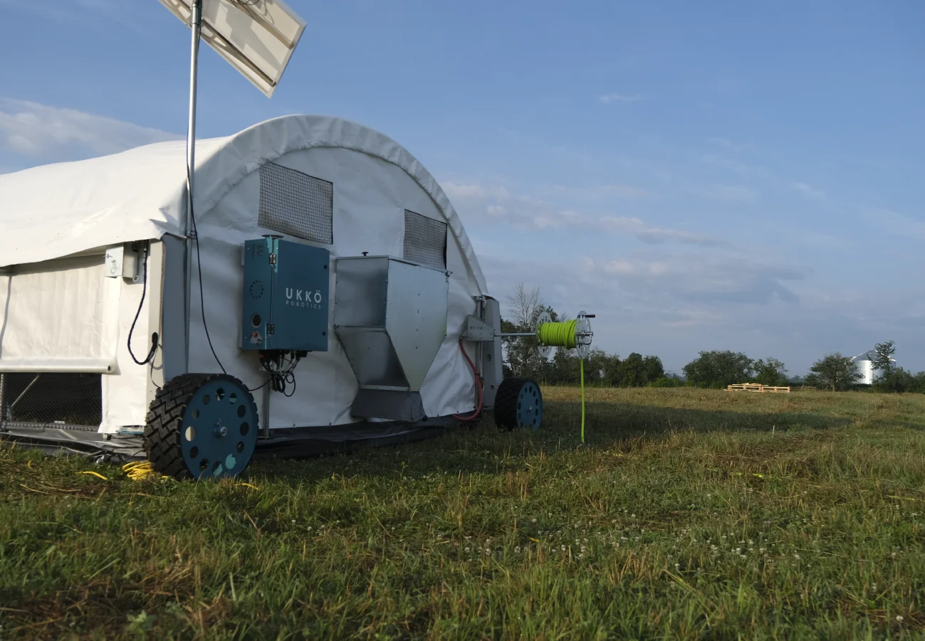 UKKÖ Robotics ROVA|BARN mobile poultry system set up in a grassy pasture with solar panel and feeding equipment attached.